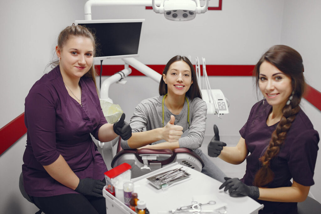 girl sitting in the dentist's office with two dentists and all are with the thumbs up