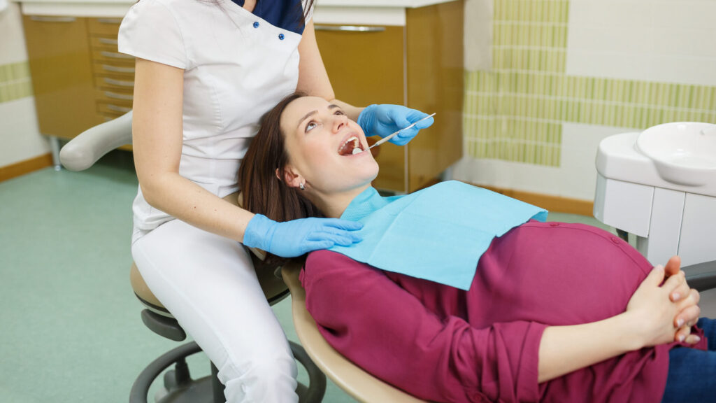 A woman seated in a dentist's chair with her mouth open and the dentist, standing behind her.