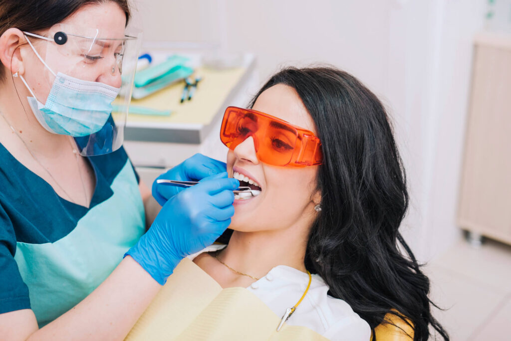 The picture shows a dentist and a patient. The dentist is wearing a mask and gloves and is holding a dental tool.